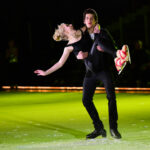 Pair performing lift under green rink lighting