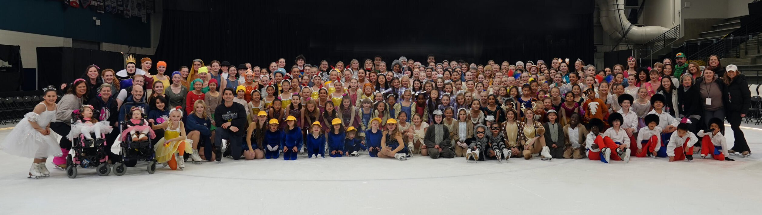 Large group of children in costumes on ice rink.